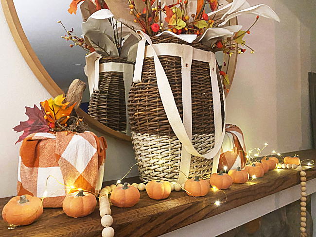 a mantel with a basket and a row of pumpkins with fairy lights