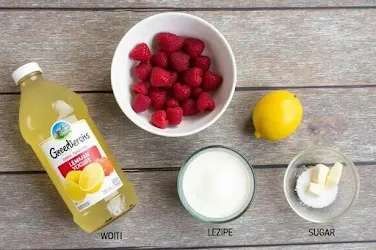 Ingredients for Raspberry Lemonade Yogurt Ice Pops, including raspberries, lemonade, Greek yogurt, and sugar, arranged on a wooden table."