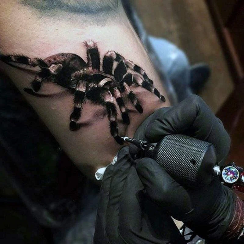 Imagen de las manos de un tatuador tatuando una tarántula