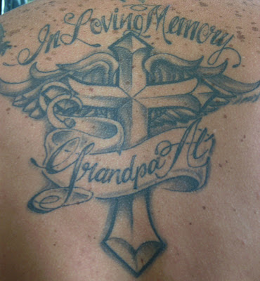 A heart with wings and cross tattoo at man's back.