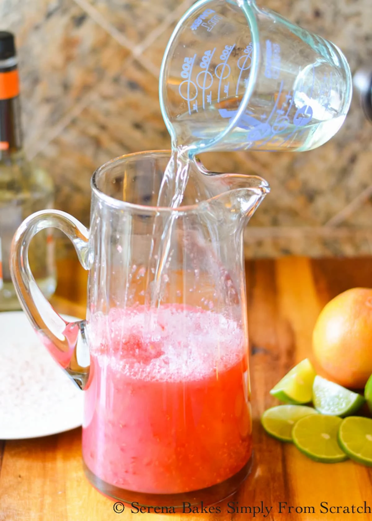 Tequila and Triple Sec being poured into a glass pitcher of Raspberry Margaritas.