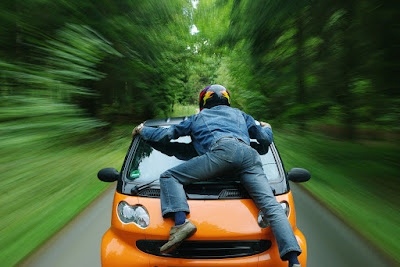 Man wearing helmet on top of small orange moving car