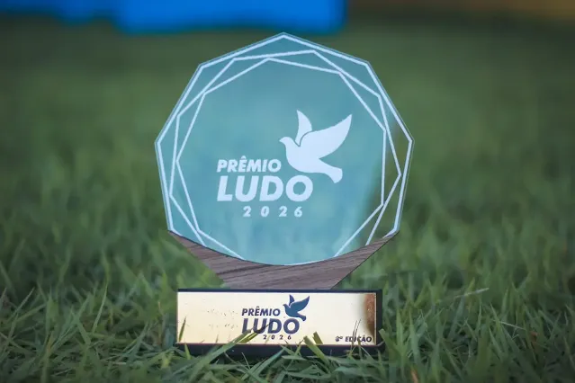 Troféu do Prêmio Ludo frontal de ângulo lateral, com a base de madeira dourada e gravação do nome do prêmio em destaque