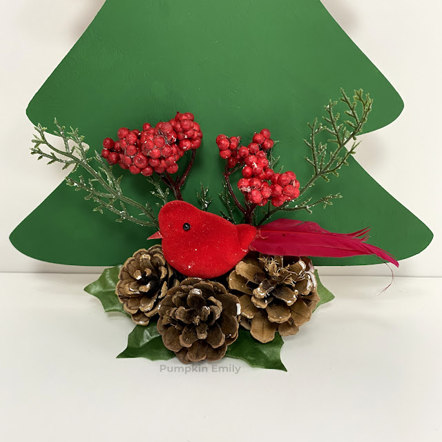 A red bird, pinecones, and berries on a the bottom of a wood Christmas tree.