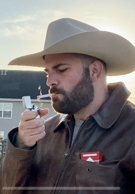 3/3 Handsome man wearing a brown leather jacket lighting a cigarette wearing a cowboy hat