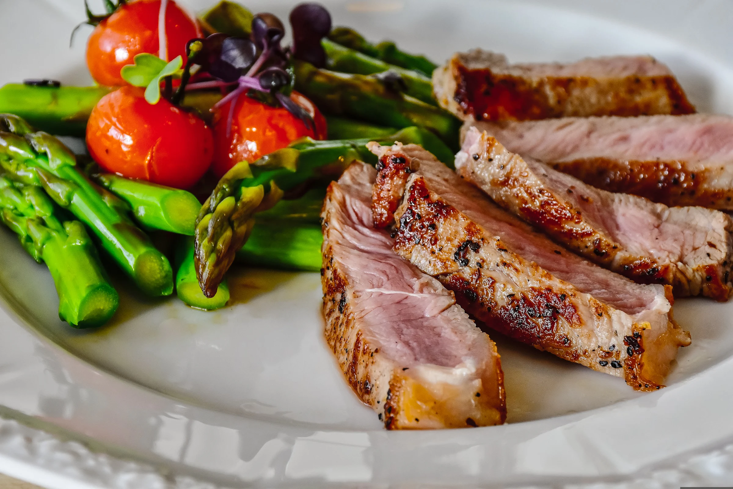 A plate with well-cooked steak slices, vibrant asparagus, and whole ripe tomatoes, representing a nutritious and balanced meal for improving physical health.