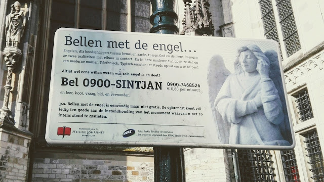 Bord dat staat bij de Sint Janskathedraal in Den Bosch: Bellen met de engel..., met een telefoonnummer erbijl.