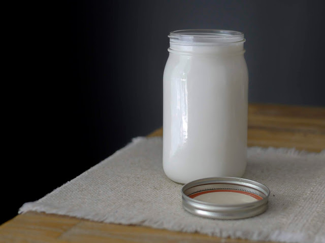 coconut milk in a mason jar sitting on a jute table runner on a wood table with a black background