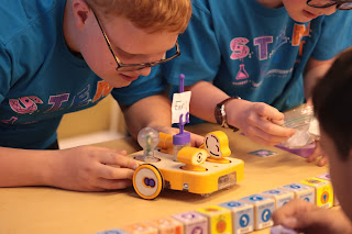 Male middle school student works on a Kibo robot. He is scanning the program blocks to the robot. 