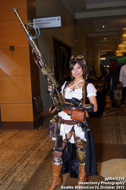 Woman wearing steampunk costume (gingham dress, boots, belt, goggles) with a big steampunk gun (steampunk weapon diy)