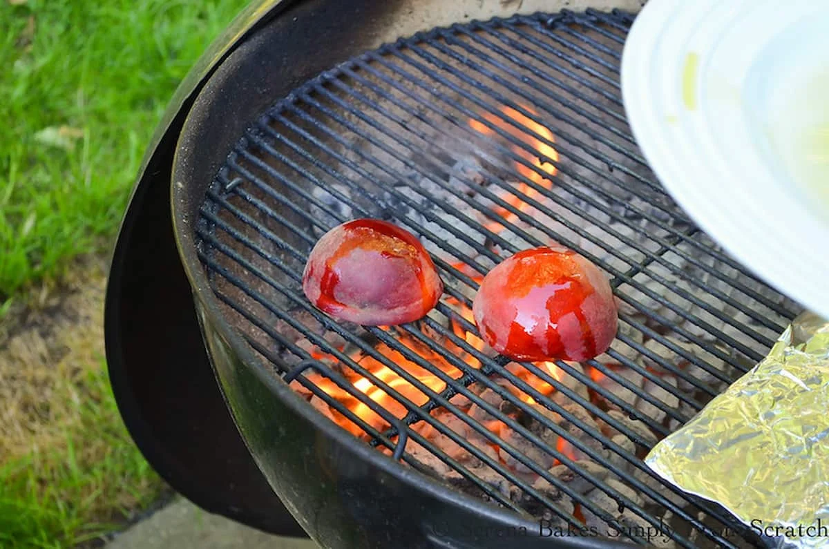 Peaches cut side down on a charcoal grill.