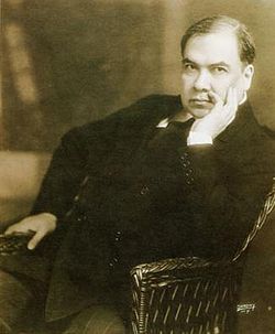 El poeta Rubén Darío sentado en una silla con la mano izquierda en el rostro y la derecha sobre su muslo derecho