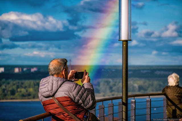 Мужчина фотографирует на телефон на фоне радуги