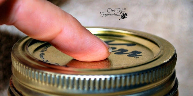 A woman's finger checking the seal on a half-pint jar of jam.