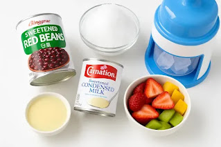 Korean bingsu ingredients including canned sweet red beans, condensed milk, fresh fruit, and a hand-crank ice shaver