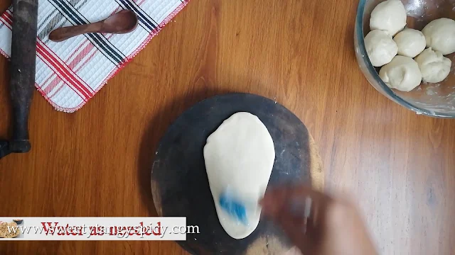 Applying water on top side of rolled butter naan dough.