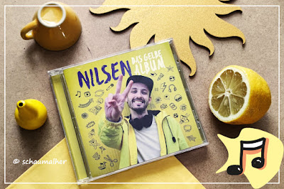 gelbe Utensilien wie Malkreide, Zitrone, Holzsonne und eine Tasse passen zum gelben Album