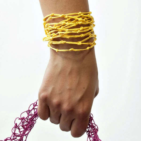 hand holding purple paper twine handle and wearing mustard yellow knotted paper twine bracelet