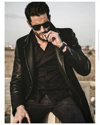Sexy gorgeous man wearing leather suit sitting outside on a bed an offense smoking a cigarette sunglasses on hair come back