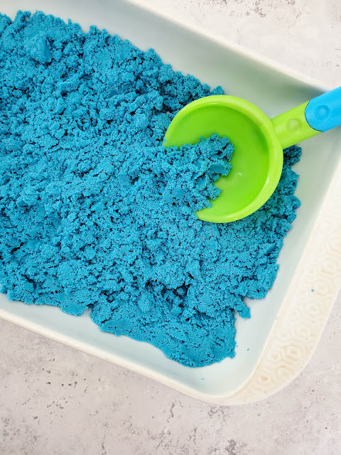 blue sand in a white dish with a green scoop.