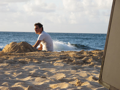 Joaquin Phoenix as Freddie Quell in The Master, sitting beside the sand sculpture of a woman, directed by Paul Thomas Anderson