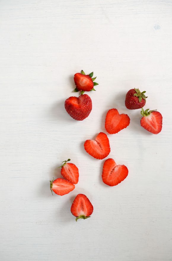 Erdbeerherzen, das sind zurecht geschnittene Erdbeerscheiben, ganze und halbe Erdbeeren liegen auf einem weißen Hintergrund.