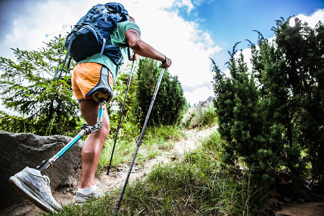 turysta z protezą nogi idący z kijami trekkingowymi po górskiej ścieżce