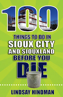 the cover of 100 Things to Do in Sioux City and Siouxland Before You Die by Lindsay Hindman, a lime green book with white and navy letters, and a picture of a riverboat imposed on the number 100