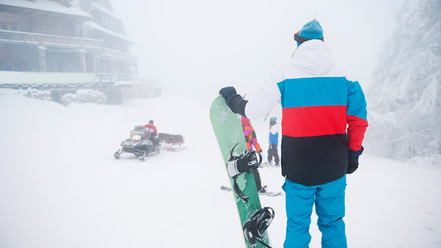 snowboarders watch a snowmobile go by pulling a sled