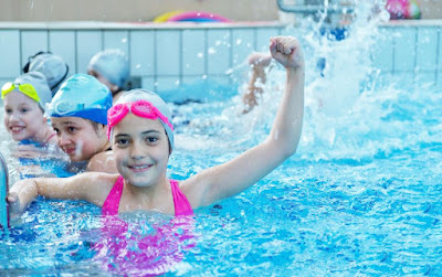 Image of a children in swimming lessons in the pool with on child giving a victory punch in the air. Managing children's behavior in the pool is important.