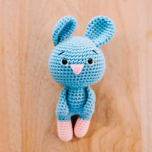 A blue and pink crocheted bunny placed on a wooden table.