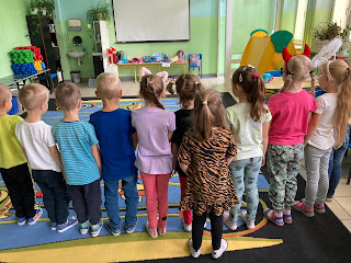 Na zdjęciu grupa dzieci, dzieci stoją, odwrócone są w stronę fotografa tyłem, w tle widnieją zabawki.