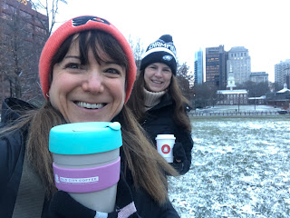 A selfie of me and Donna, holding up coffee cups, wearing Flyers and Eagles hats, in front of a snowy Independence Hall.