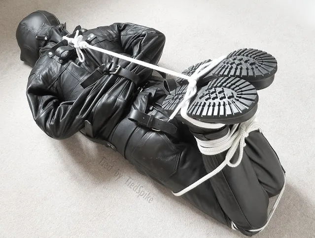 8/12 man bound completely in leather with a hood and straightjacket Face down on the floor with hand side behind back to feet