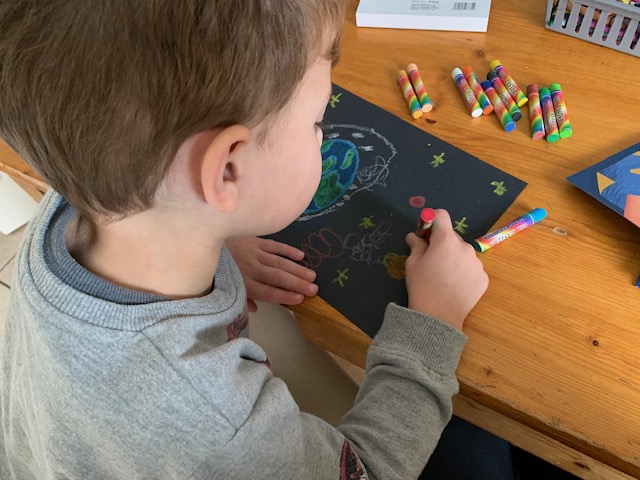 Boy drawing a space scene on black card, using pastels