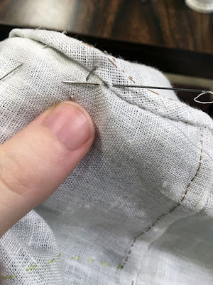 A close-up of finishing a flat-felled seam in white linen with tan thread.