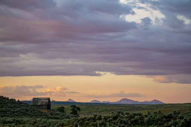 Sunrise over a prairie with a dilapidated wooden building in the distance.