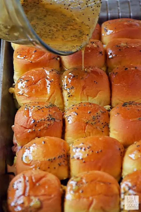 Pouring buttery Dijon glaze on top of assembled ham and cheese sliders