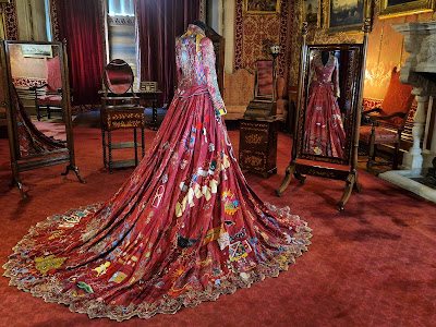 a heavily embroidered red, full length dress on a mannikin, in a large timbered hall