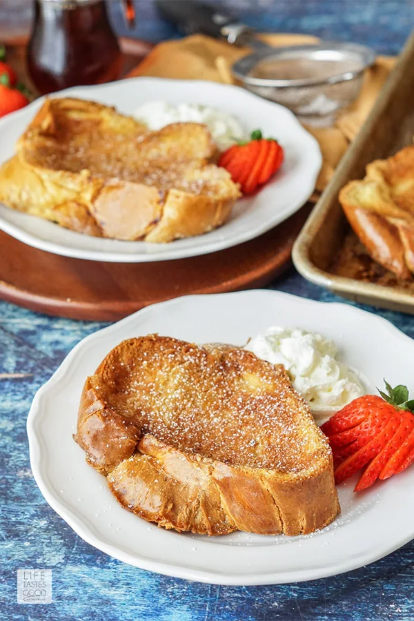 Breakfast table with creme brulee french toast on white plates with whipped cream and strawberries