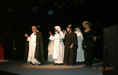 Grupo “Teatro Biblio”. Obra de teatro: Sermón de Adviento, 17 de mayo del 2011.  Sala Ravelo del Teatro Nacional, Plaza de la Cultura “Juan Pablo Duarte” en la Avenida Máximo Gómez, Santo Domingo, Distrito Nacional. Escenario a oscuras. Al frente el grupo de actores vestidos como frailes (túnica o hábito, escapulario con capuchón para la cabeza, correa o cíngulo, cogulla o túnica amplia con grandes mangas). En primer plano, Iván García Guerra, con hábito blanco con amplia capa negra por encima, un solideo o pequeño gorro redondo negro que solo cubre la coronilla. Sus manos en alto y su cabeza baja, como orando. Un paso más atrás los demás: primera línea, de izquierda a derecha: Alexis Román, hábito blanco con capucha en su cabeza, manos en alto y cabeza baja, actitud de oración; Hugo Albuerme, amplio ropaje largo de color negro con amplias mangas largas con un sombrerito; un poco apartada, a la derecha, vestida de negro (con blusa larga y pantalón largo), la narradora Carmen Rosa Estrada. Detrás de Alexis y Hugo, tres frailes (Arlene Severino, María Esther Abreu, Amarilis Méndez) con hábito blanco y capucha en sus cabezas. El grupo está iluminado por un reflector. 