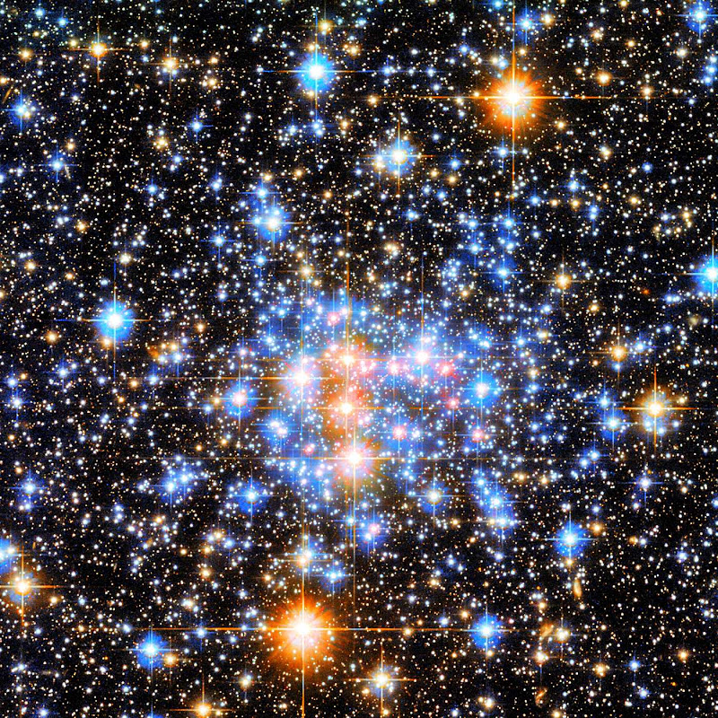 Um grande número de estrelas brilhantes, cada uma com uma forma de cruz que se estende a partir do seu centro. No centro há uma densa coleção de estrelas em primeiro plano. Cinco são laranjas e o restante são azuis. O fundo preto é preenchido com pequenas estrelas - a maioria delas, porém, maiores que um único ponto.