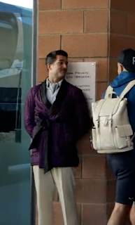 Milo McCabe aka 'Troy Hawke' of the 'Greeters Guild' at the entrance of the Manchester City FC training location. Troy is wearing a purple, silk Smoking Jacket, a cravat and cream coloured flannel trousers.