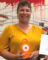 Rachel is holding her trophy, which is an orange and white representation of the Open Access open padlock, and smiles happily.