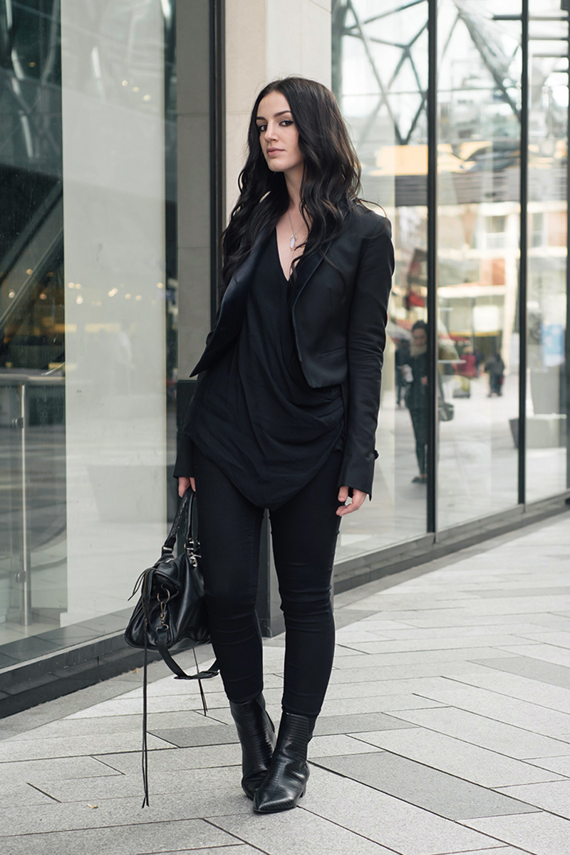 stylish young woman in total black outfit is posing for the camera on a street