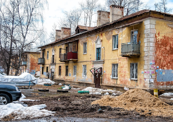 Куча песка в грязи на фоне старого и обшарпанного желтого здания