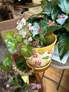 A begonia plant in a yellow-rimmed pot, with a stem of tiny pink flowers.