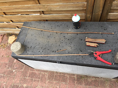 Rotstein Terrasse. Darauf eine Plastikkiste mit schwarzem Deckel. Darauf liegen zwei längere Äste und zwei kleine Waggons neben einer Rosenscheere. Auf den Waggons sind schon gekürzte Äste zu sehen.