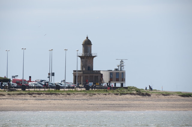 Small lighthouse and radar installation next to parked cars.