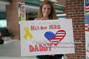 A wife waits for her husband to exit the plane, while holding a sign